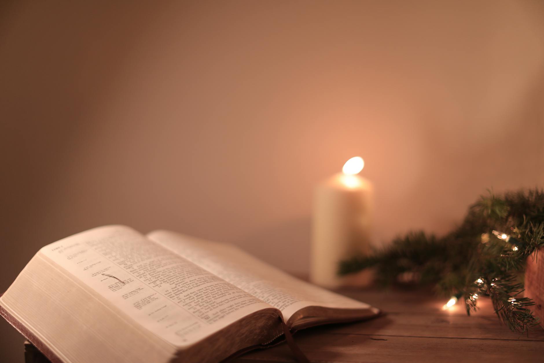 a bible on a wooden surface with pine leaves and christmas lights